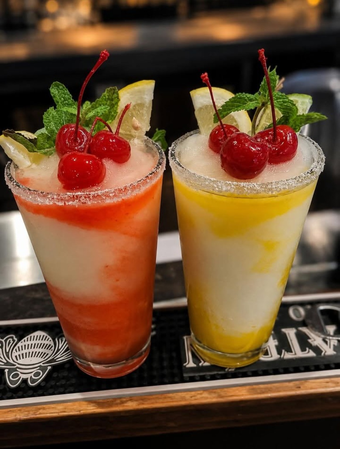 Two frozen daiquiris with salted rims, mint, citrus and cherries